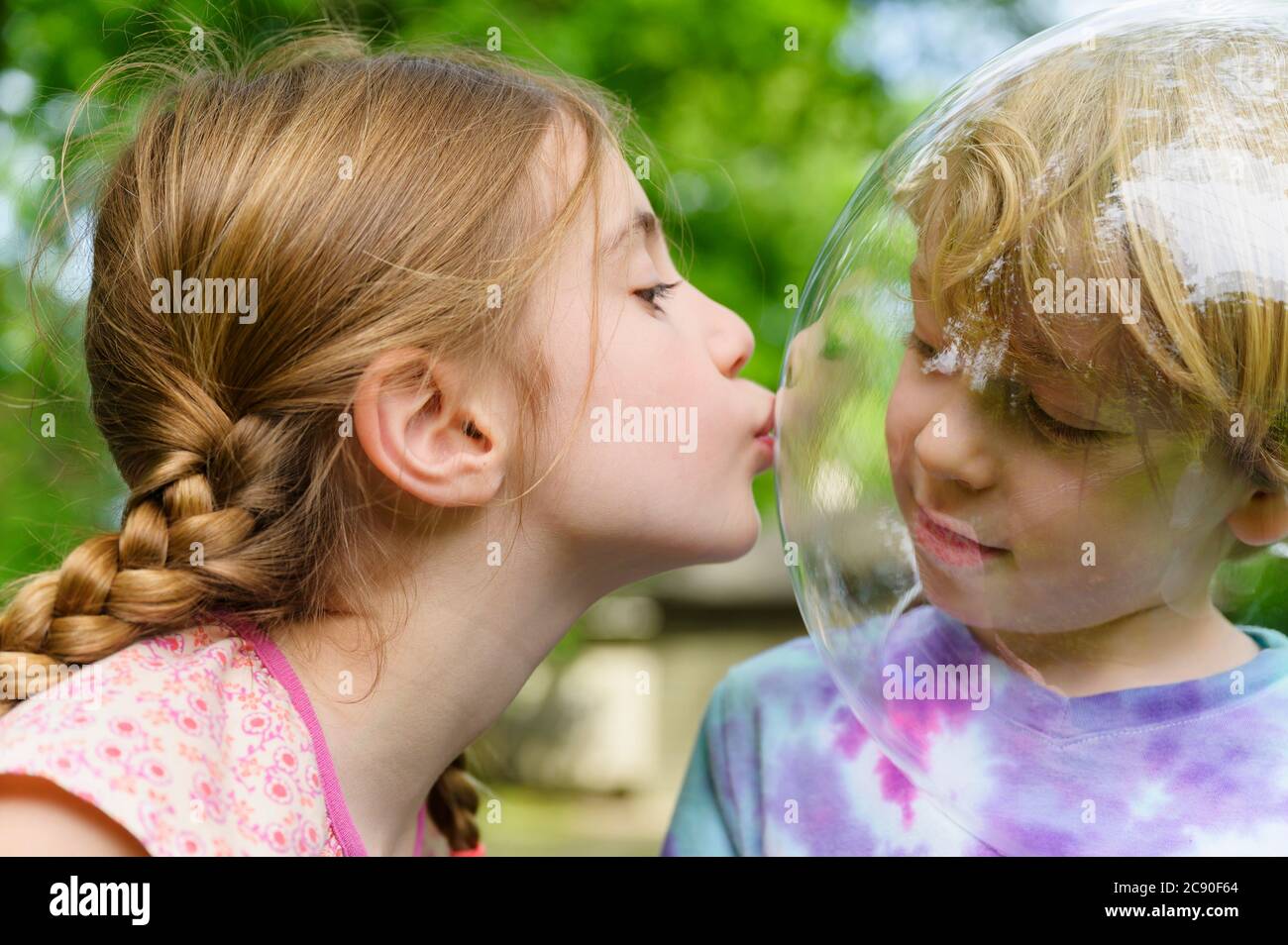 Girl kissing boy wearing bubble to socially distance Stock Photo