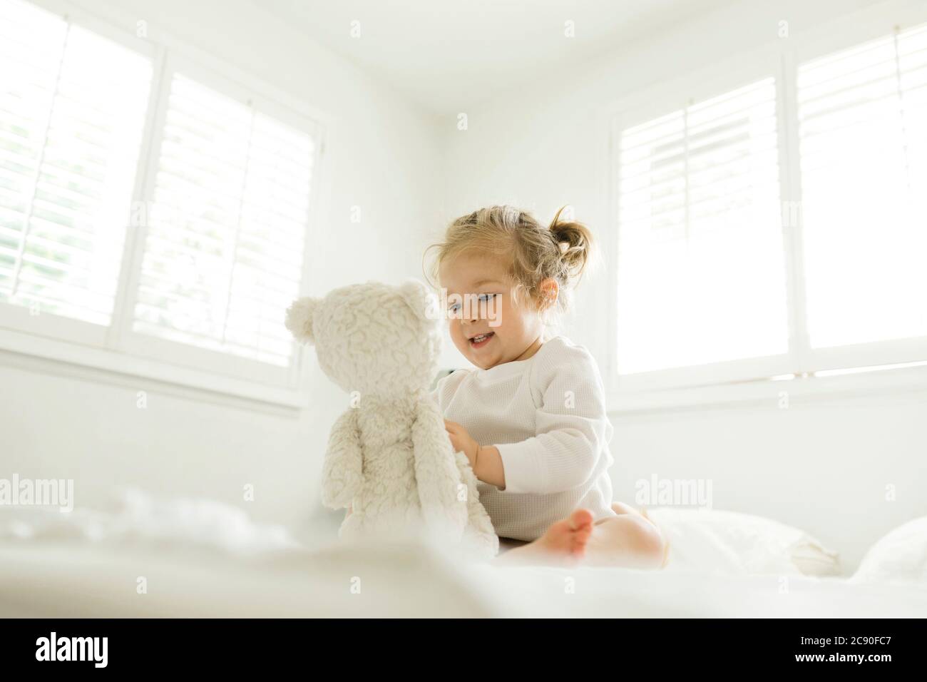 Toddler girl playing on bed with her teddy bear toy Stock Photo