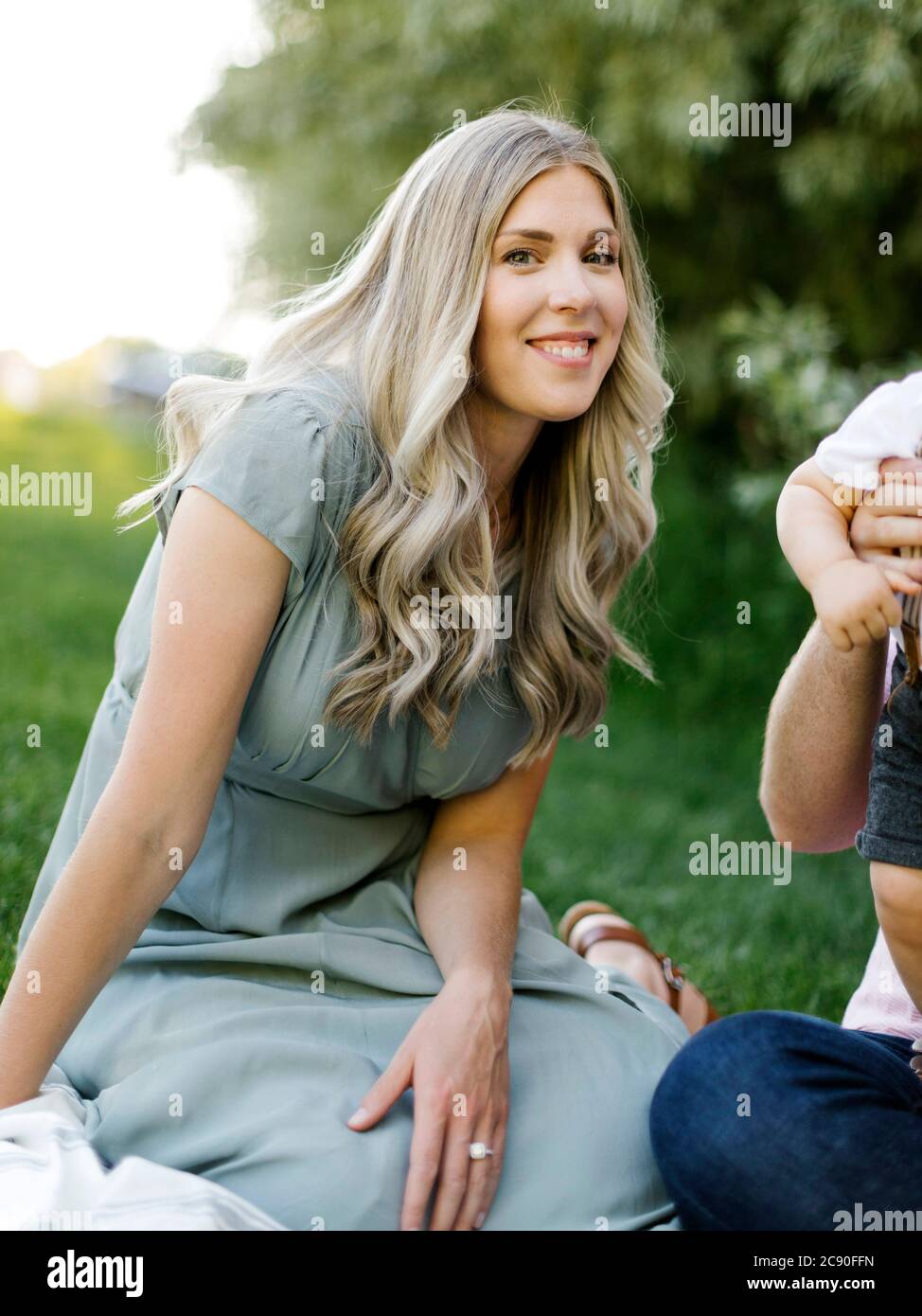 Outdoor portrait of smiling woman sitting o grass with her family nearby Stock Photo