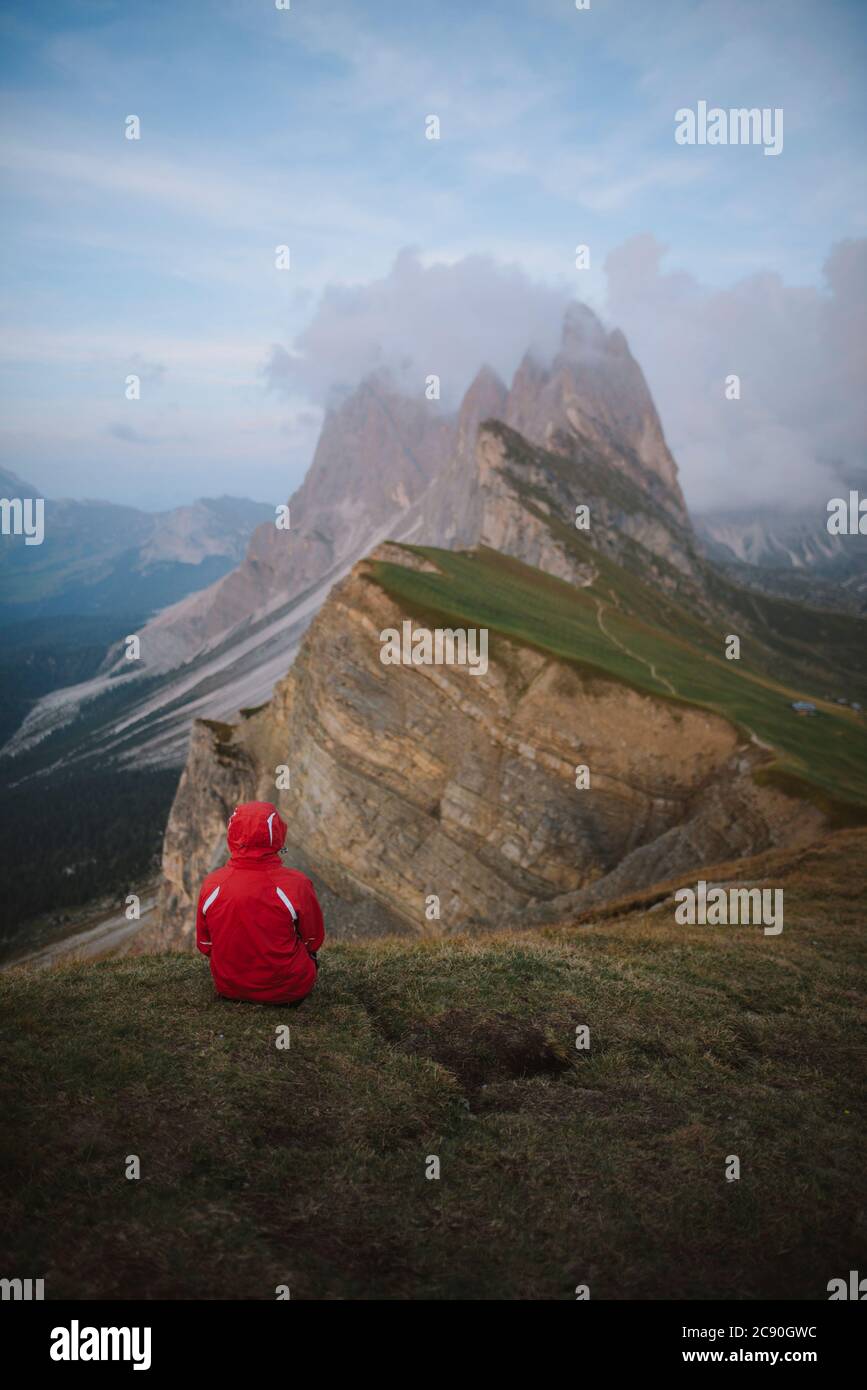 Italy, Dolomite Alps, Seceda mountain, Person sitting on grass looking at scenic view of Seceda mountain in Dolomite Alps Stock Photo