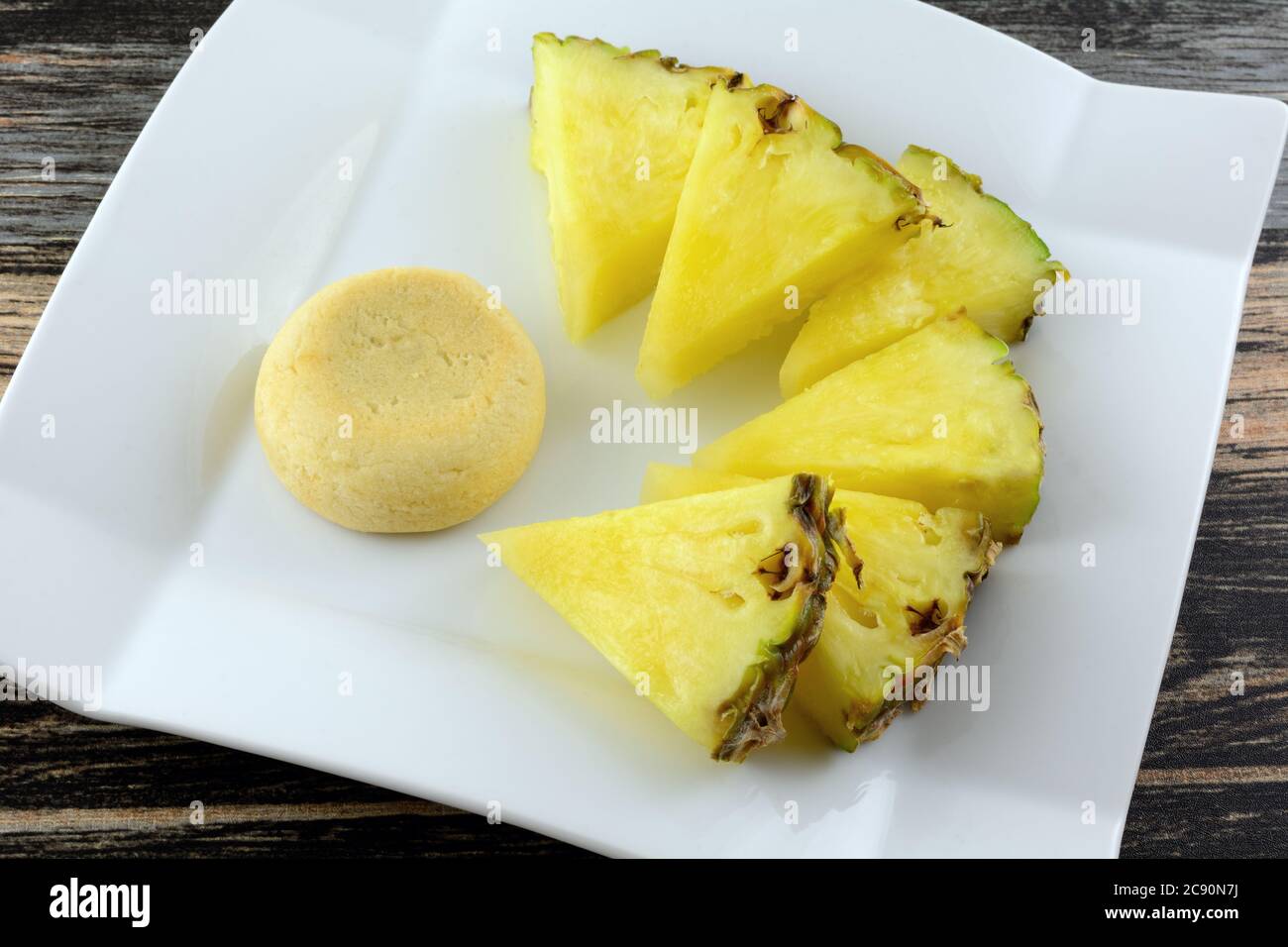 Pineapple shortbread cookie with pineapple filling and fresh pineapple wedges on white dessert plate Stock Photo