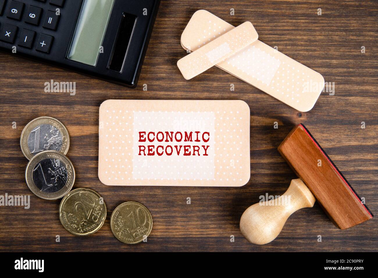ECONOMY RECOVERY concept. Note sheet like medical plaster. Euro money,  wooden stamp and calculator on a dark wooden table Stock Photo - Alamy