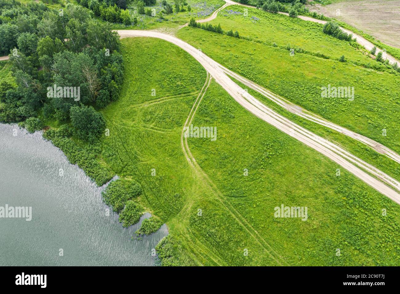 countryside landscape in summer. rural dirt road on green meadow near lake. birds eyes view Stock Photo