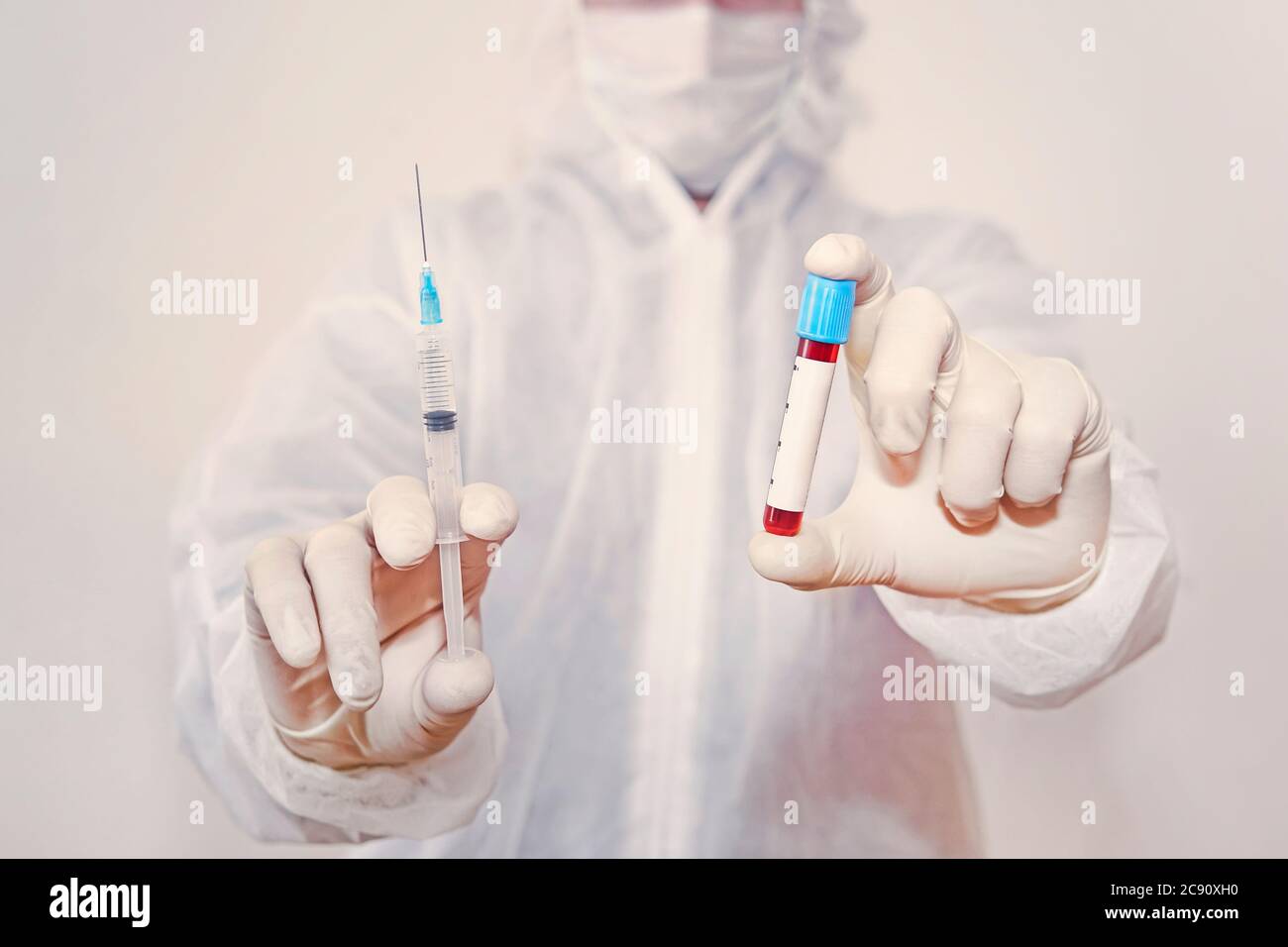laboratory employee holds a syringe with a vaccine and a test tube with blood in his hand. Empty white label on a glass blood bottle for design or Stock Photo