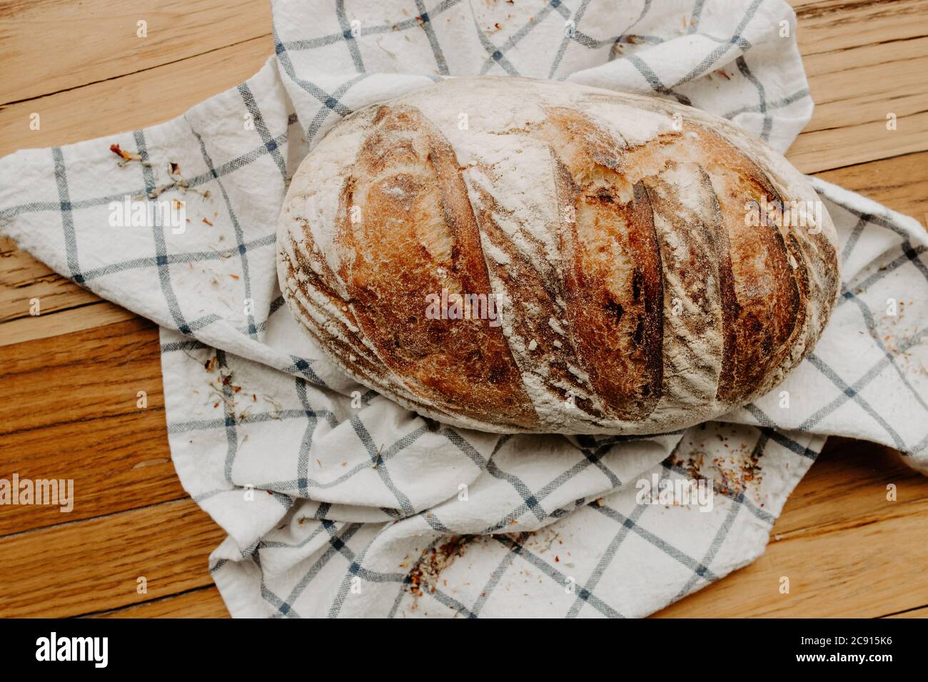 Home made Sour dough bread cooling on a tea towel which is on a wooden chopping platter board, wild dried flowers are sprinkled around Stock Photo