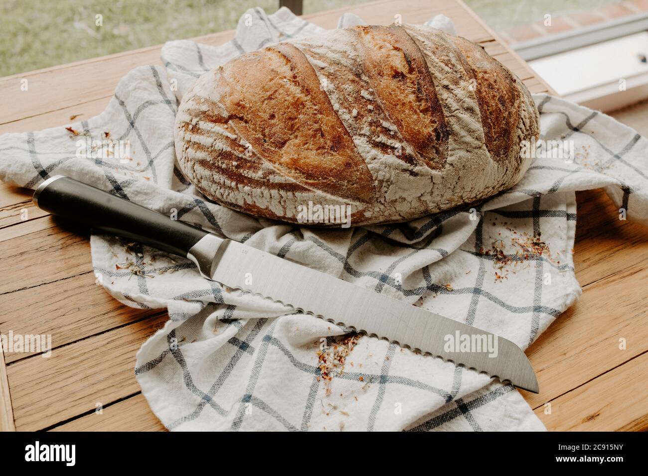 Home made Sour dough bread cooling on a tea towel which is on a wooden chopping platter board, wild dried flowers are sprinkled around Stock Photo