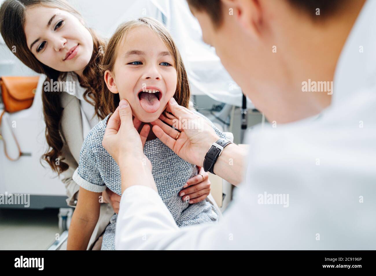 Throat sick little girl in being examined by pediatrician, sitting on mom's lap Stock Photo