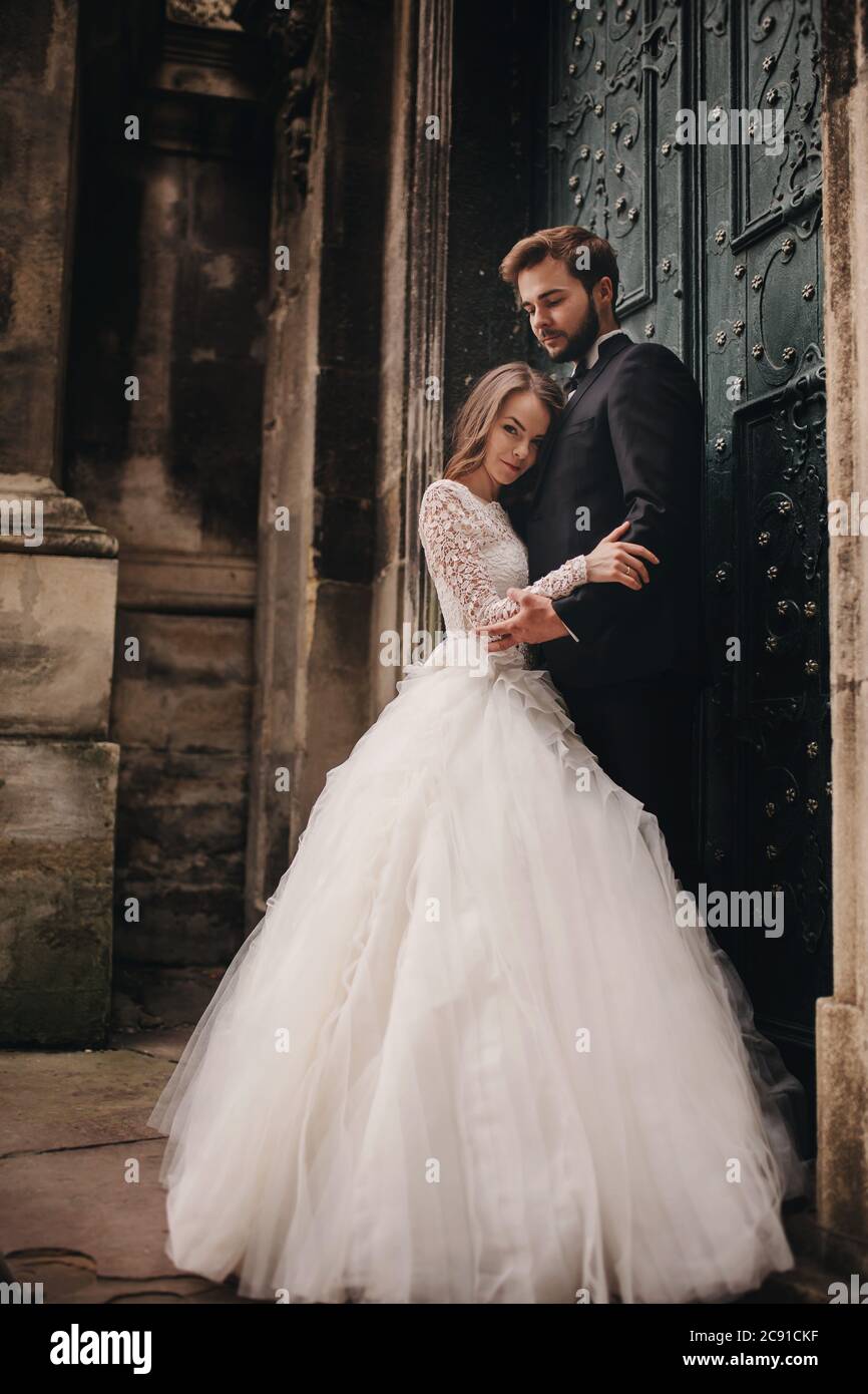 Wedding couple hugs near the vintage green door. Stone walls in ancient town background. bride with long hair in lace dress and groom in suit and bow Stock Photo