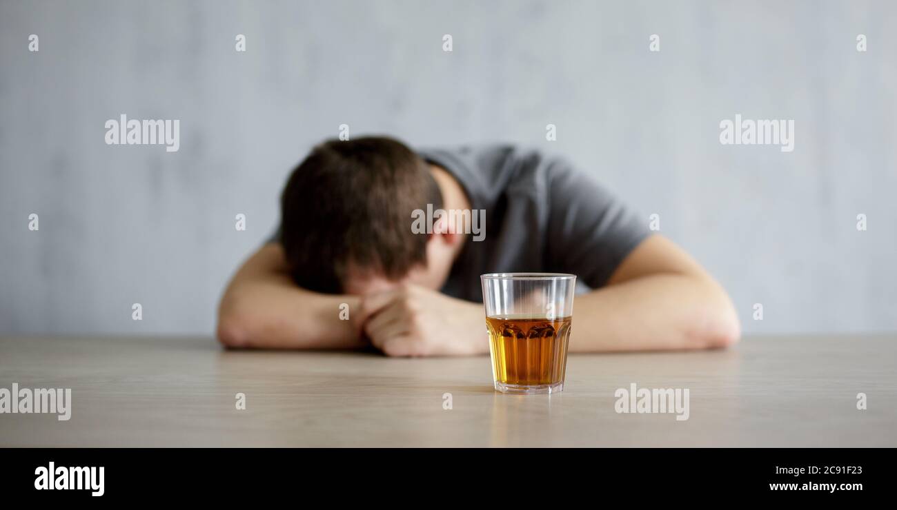 alcoholism concept - drunk man lying on the table and glass of whiskey over gray wall background Stock Photo