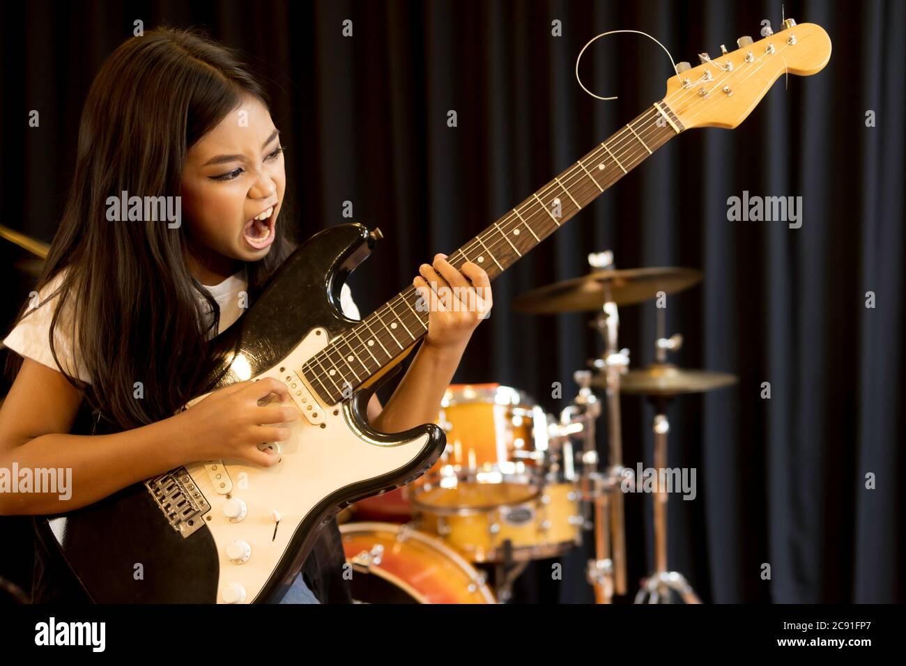 A cute young Asian elementary school girl with long hair playing with serious electric guitar in rock songs. Stock Photo