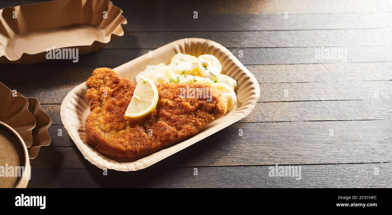 Takeaway fried battered fish with French fries on a cardboard disposable plate over a rustic wooden table with copyspace viewed high angle in a panora Stock Photo
