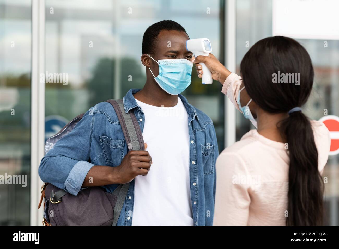 Airport Worker Checking Black Male Passenger Temperature With Electronic Thermometer After Arrival Stock Photo