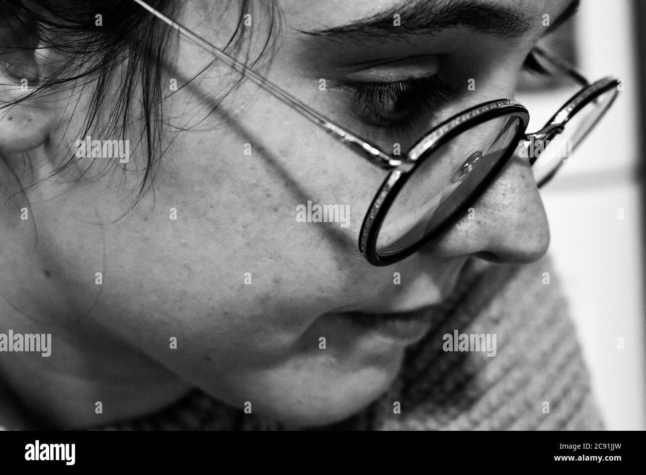 Greyscale shot of the side profile of a thoughtful young female with glasses Stock Photo
