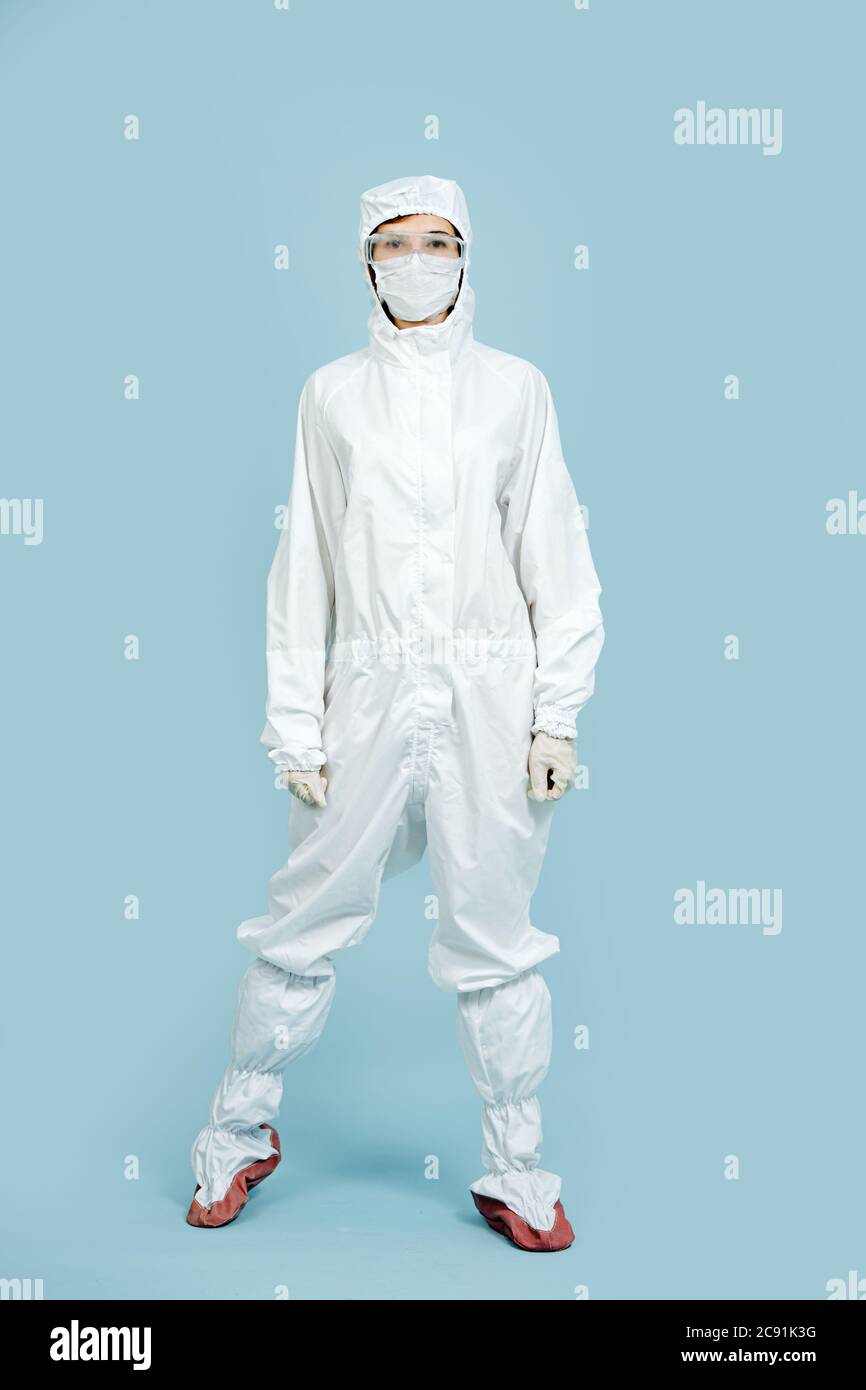 Doctor posing in a white gown covering all skin over blue backgound. Mask on. Stock Photo