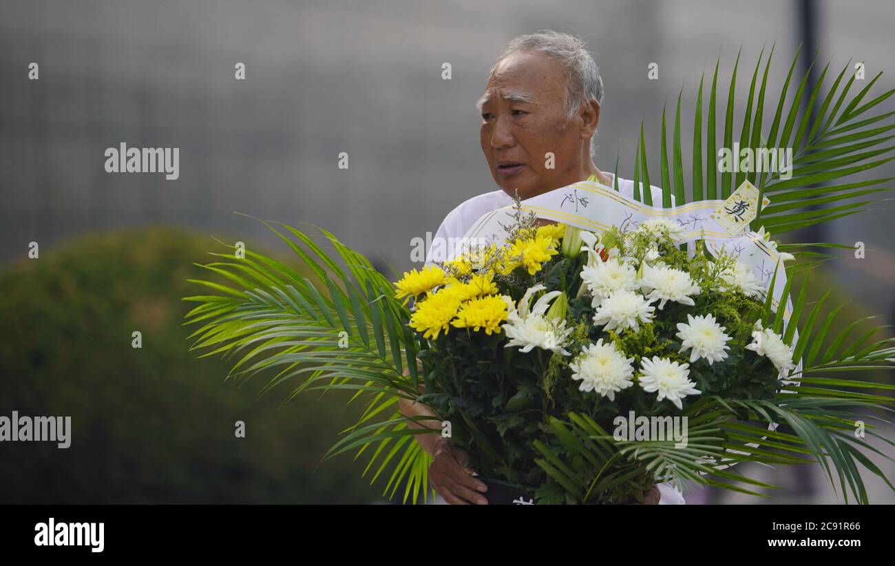 Tangshan. 28th July, 2020. A man holding a flower basket walks past a memorial wall in Tangshan, north China's Hebei Province, July 28, 2020, the 44th anniversary of the 1976 Tangshan Earthquake. Credit: Dong Jun/Xinhua/Alamy Live News Stock Photo