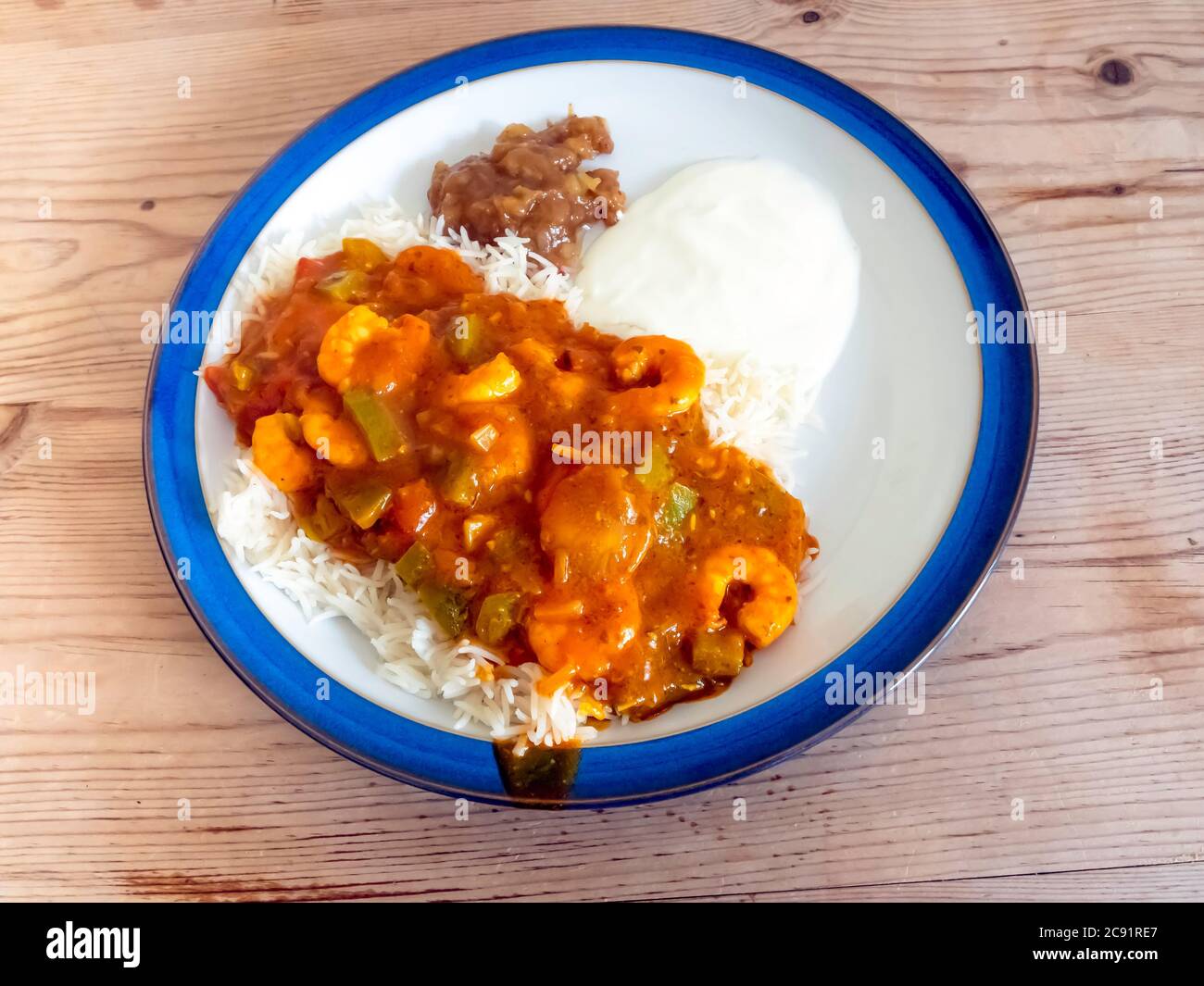 Indian style food prawn curry Jalfrezi on Basmati rice with yoghurt and mango chutney on a wooden table top Stock Photo