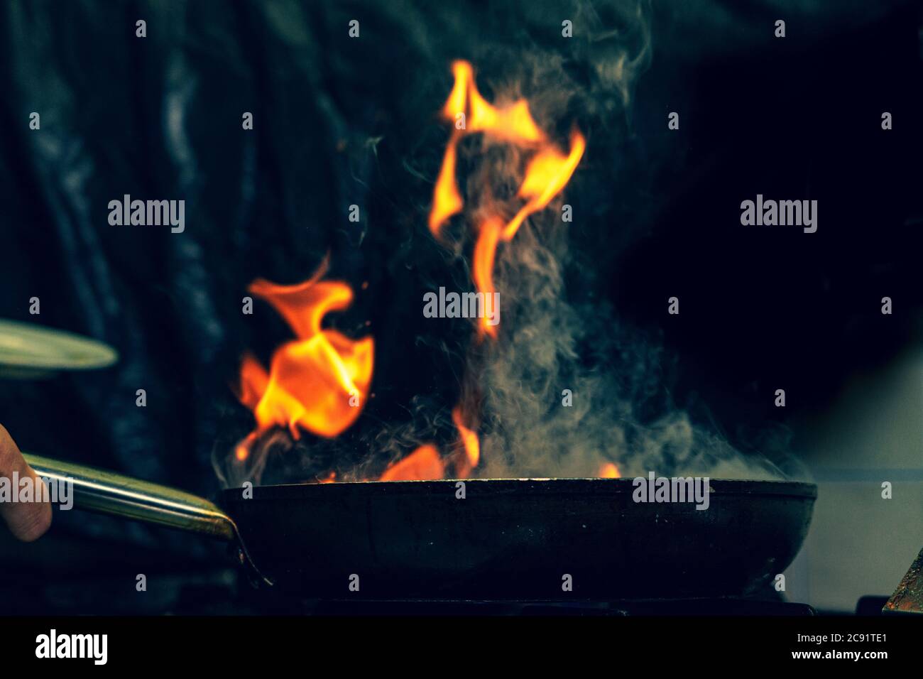 Closeup chef cooking with fire In a frying pan on blurred background ...