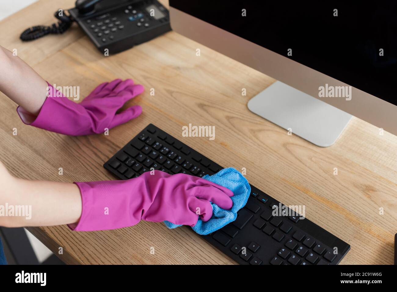 Cropped view of cleaner using rag on computer keyboard on table in ...