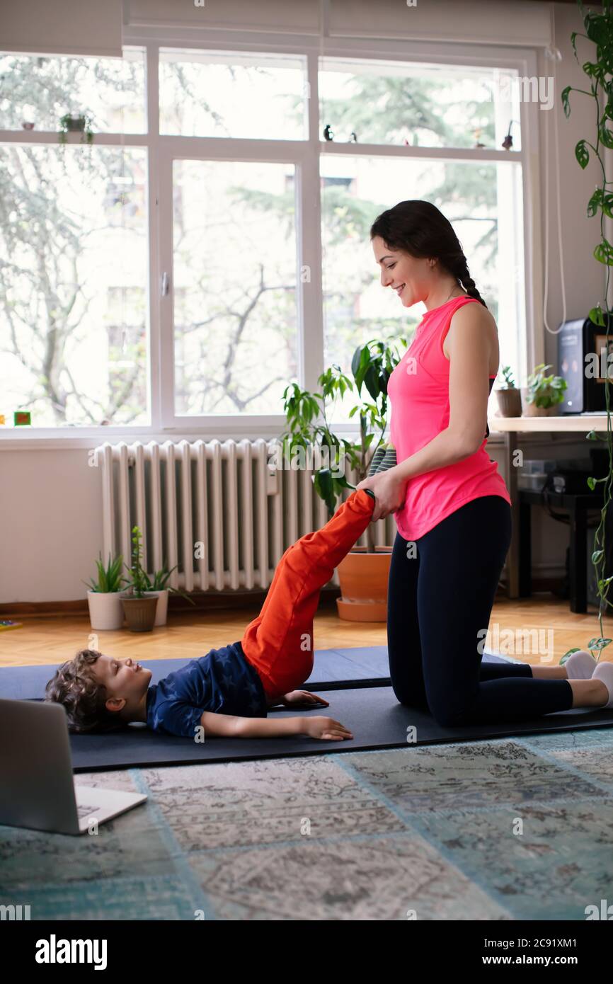 Young Mother helping her Son Exercising Pilates, Yoga, Fitness at Home in front of the Laptop Stock Photo