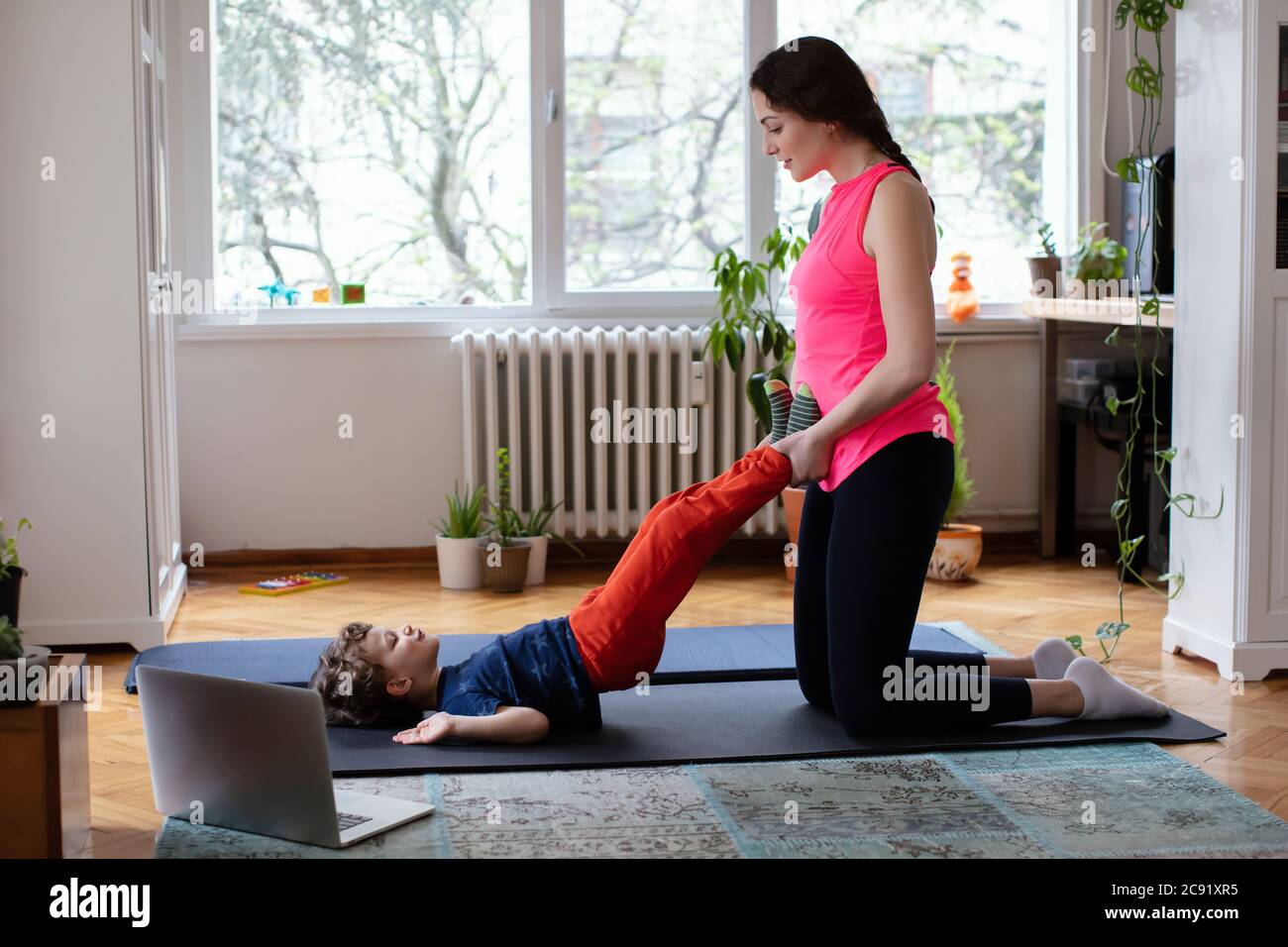 Young Mother helping her Son Exercising Pilates, Yoga, Fitness at Home in front of the Laptop Stock Photo