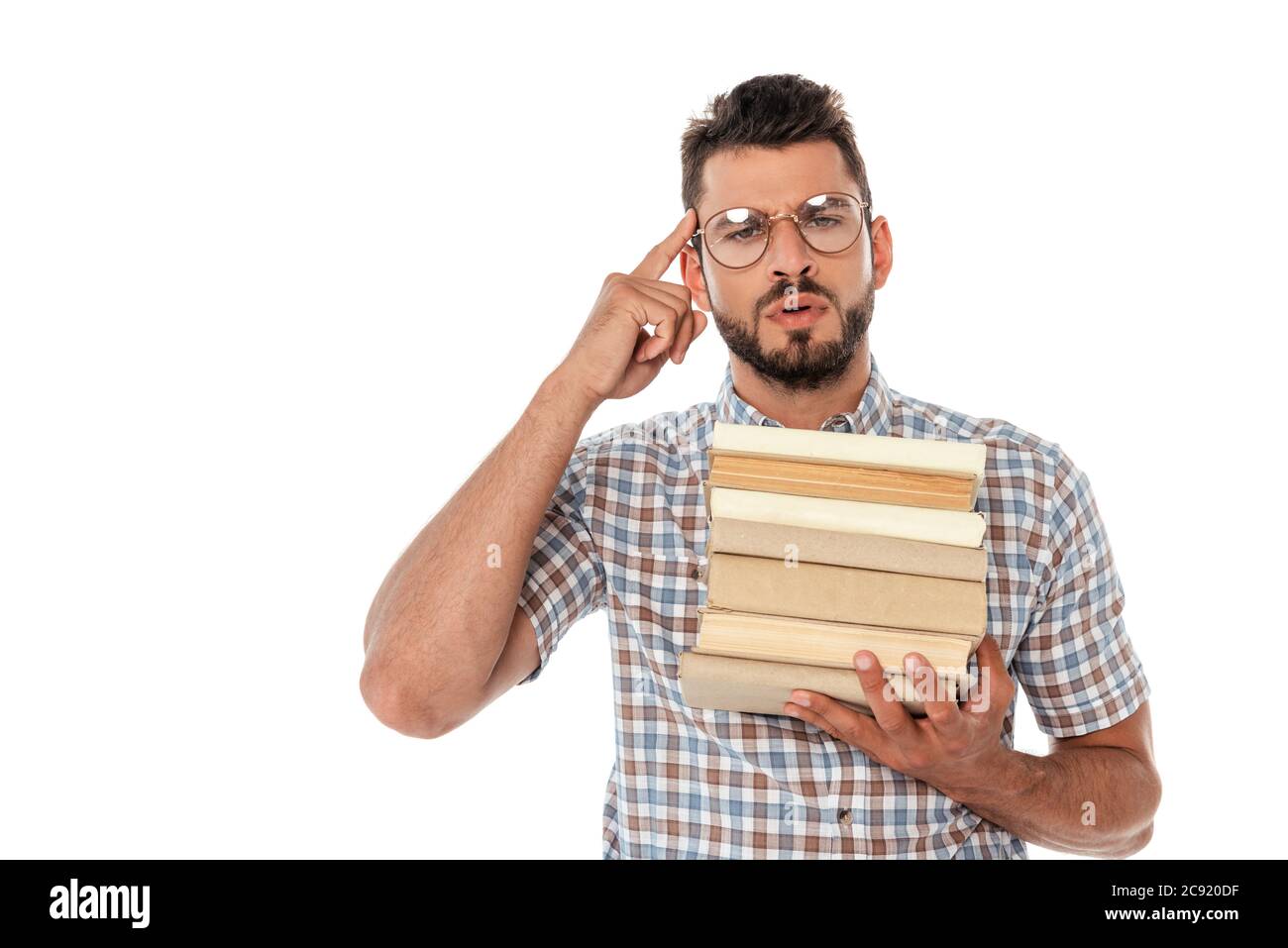 Concentrated nerd in eyeglasses holding books and pointing with finger at head isolated on white Stock Photo