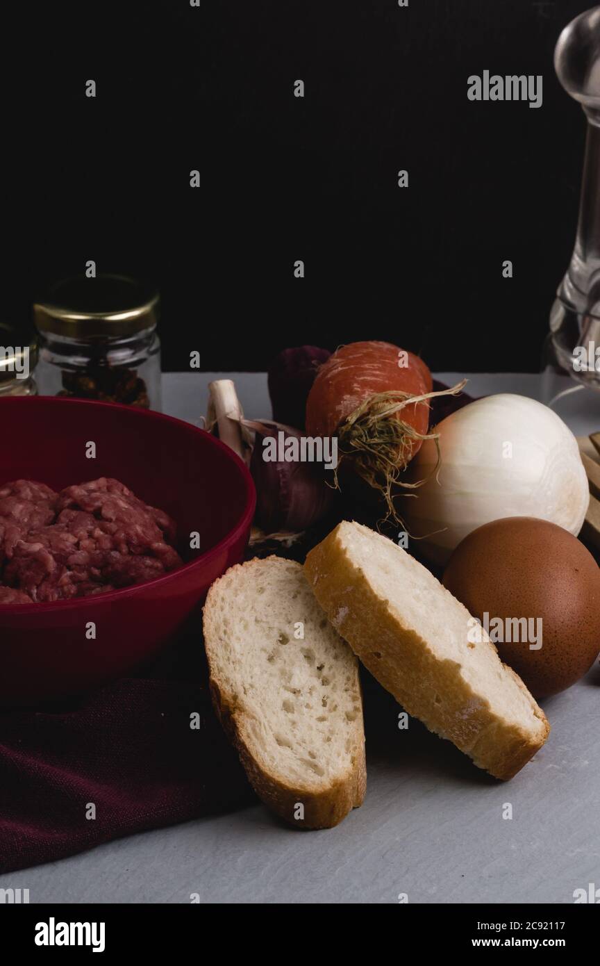 Vertical closeup shot of ingredients for preparing meatballs on a white kitchen table Stock Photo