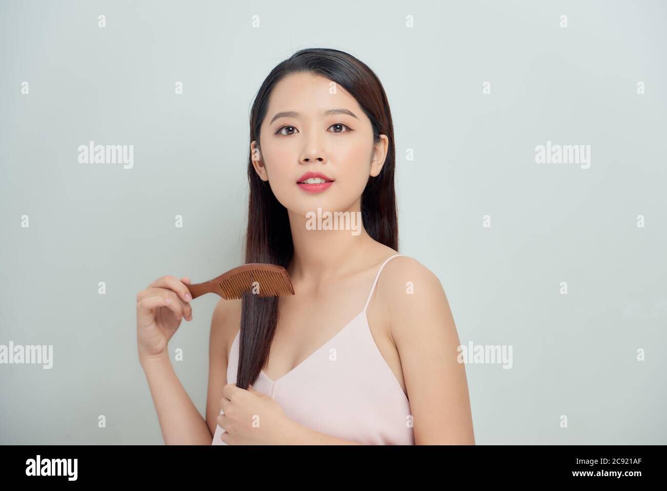 Portrait of beautiful young woman combing her hair, looking at camera and smiling Stock Photo