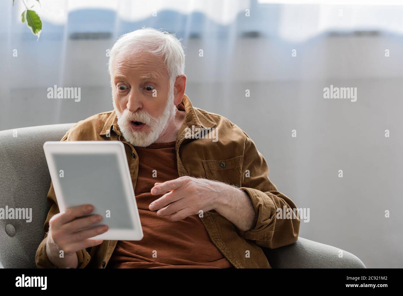 shocked senior man pointing with finger while using digital tablet Stock Photo