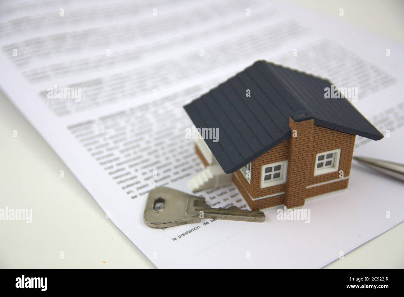 A small house on the papers for the bank of a mortgage just signed next to a pen and the key of the house. Stock Photo