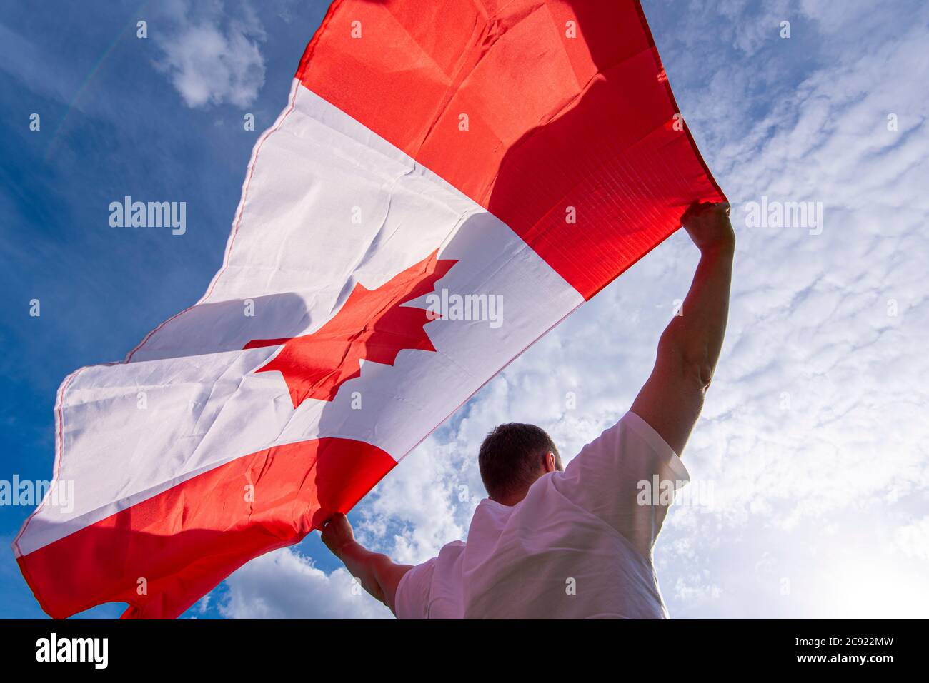 Man holding The National Flag of Canada against blue sky Stock Photo