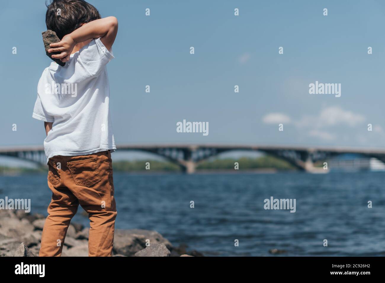 back view of cute boy holding rock near blue lake Stock Photo - Alamy