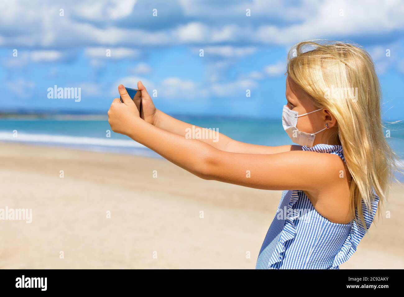 Funny girl taking selfie photo by smartphone on tropical sea beach. New rules to wear cloth face covering mask at public places due coronavirus COVID Stock Photo