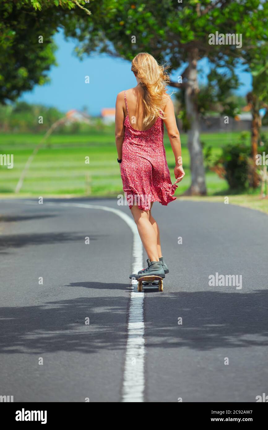 Young woman riding on skateboard. Happy woman have a fun on empty road. Active family lifestyle, outdoor recreational activities on summer holidays on Stock Photo