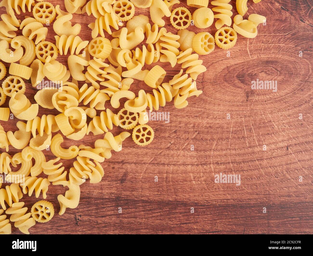Various dried pasta shapes on wood board. Pasta for salads. Stock Photo