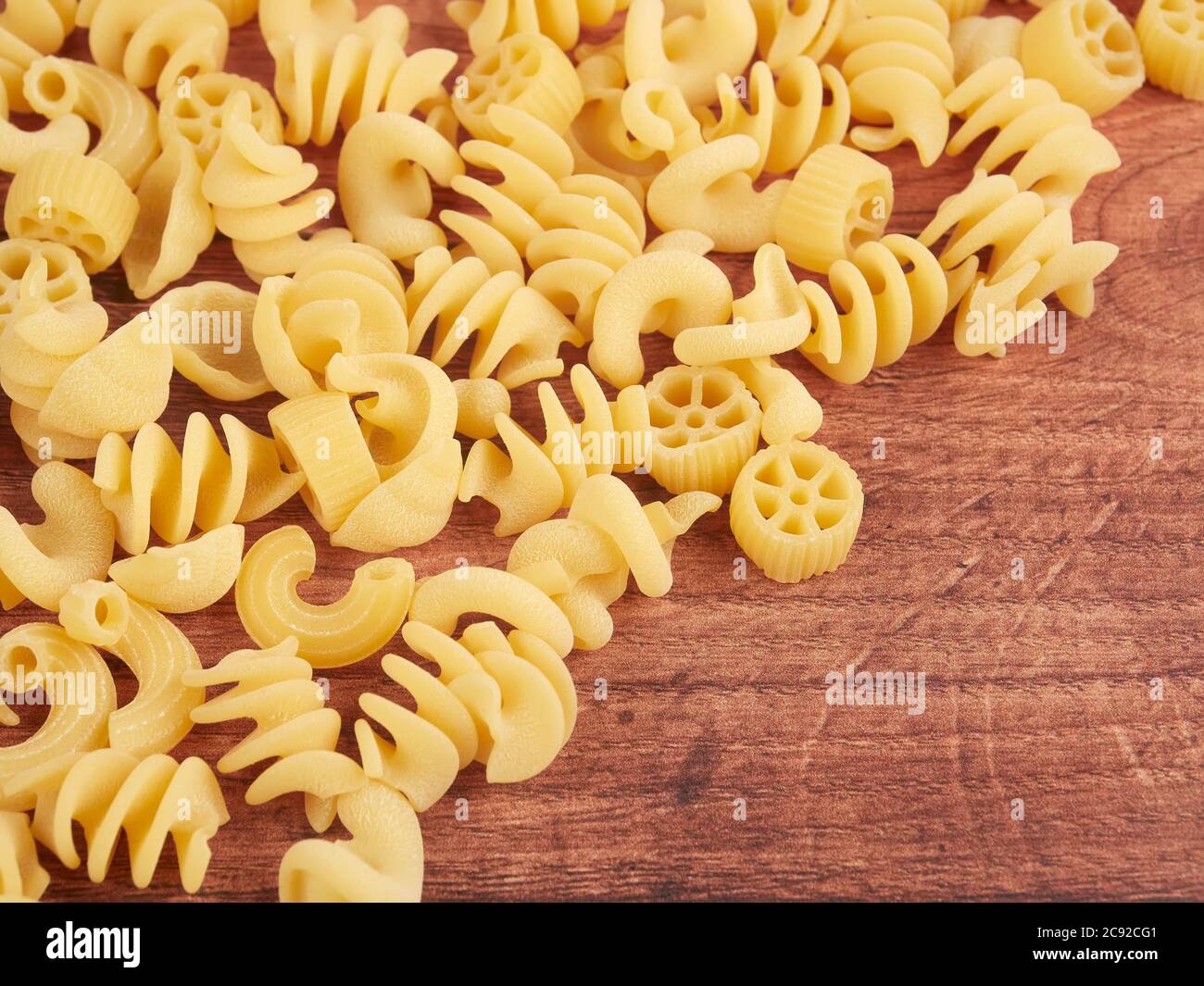 Various dried pasta shapes on wood board. Pasta for salads. Stock Photo