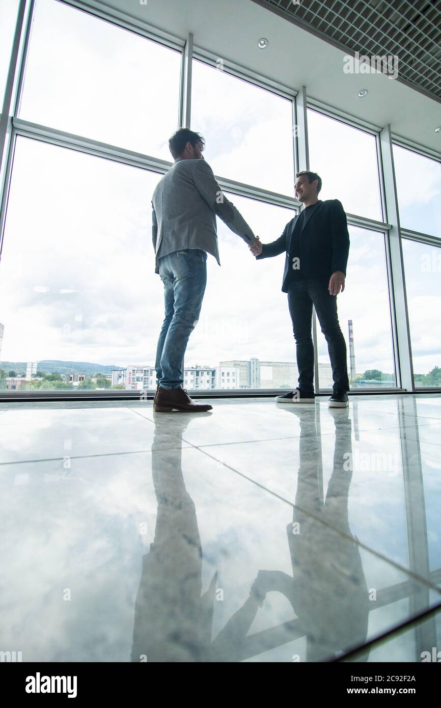 Full length side view of businessmen shaking hands in office building ...
