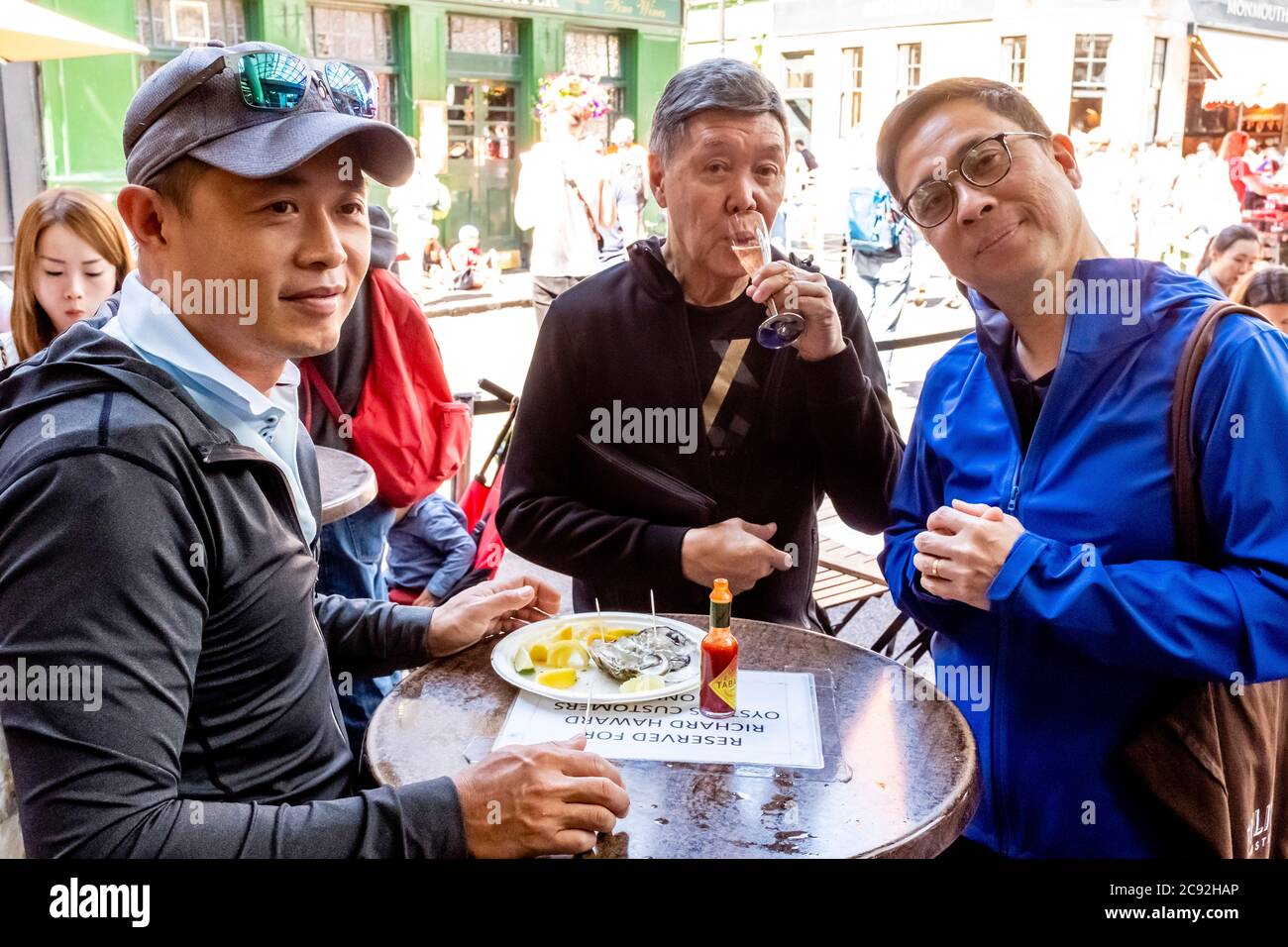 Asian People Eating Oysters At A Table In Borough Market, London, England. Stock Photo