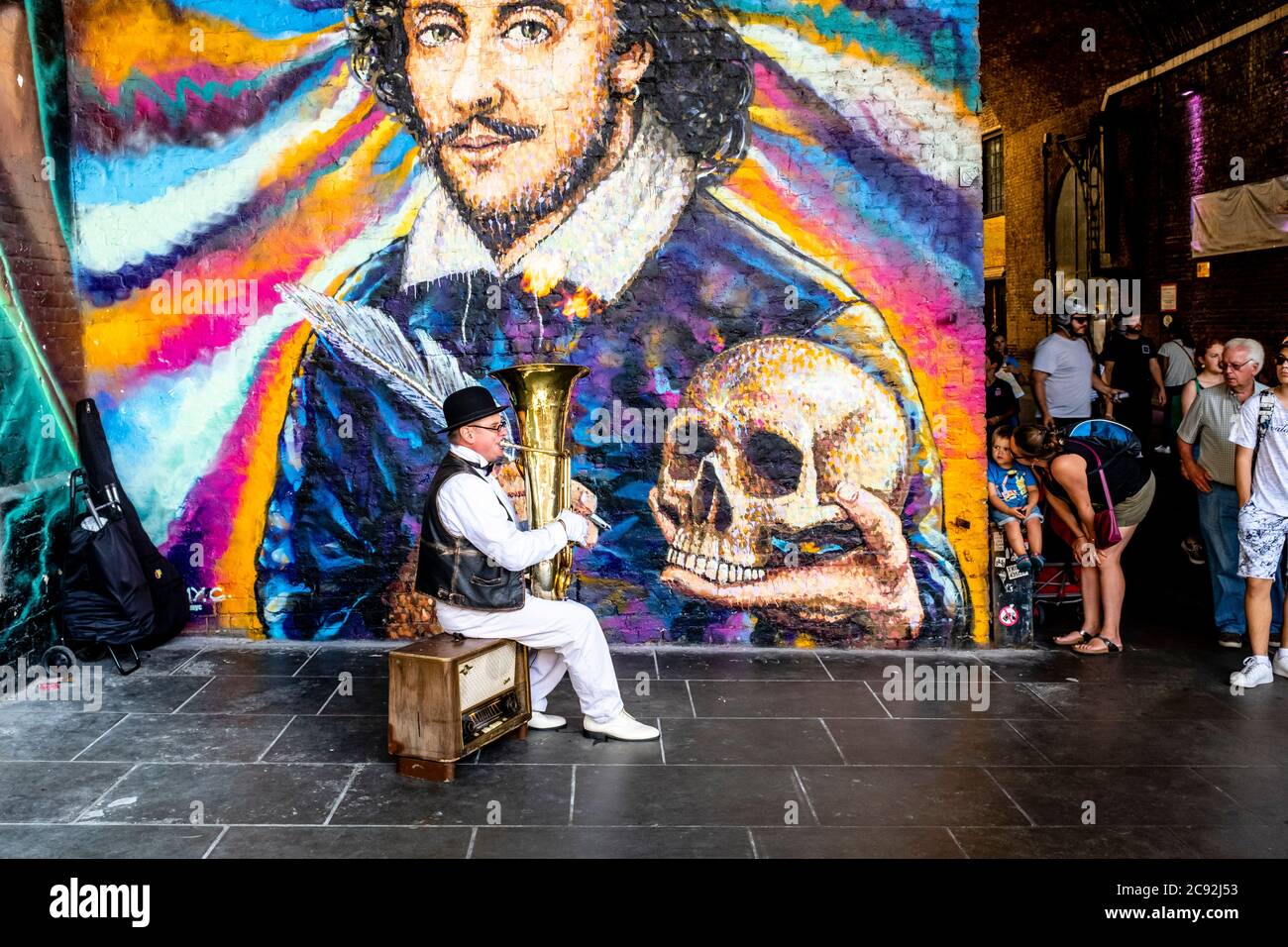 A Street Entertainer Plays Music In Front Of A Giant Mural Of William Shakespeare, Clink Street, London, UK Stock Photo