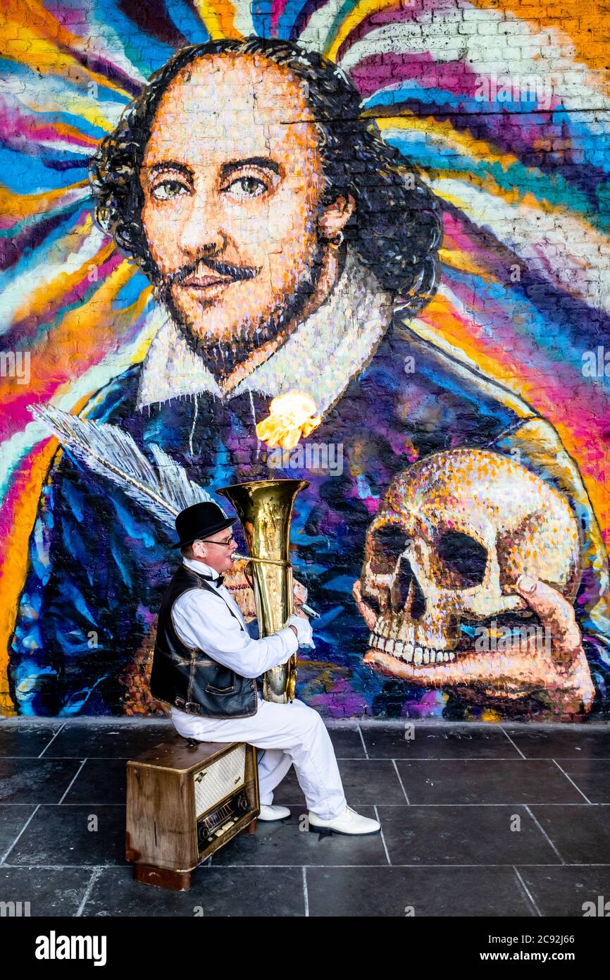 A Street Entertainer Plays Music In Front Of A Giant Mural Of William Shakespeare, Clink Street, London, UK Stock Photo
