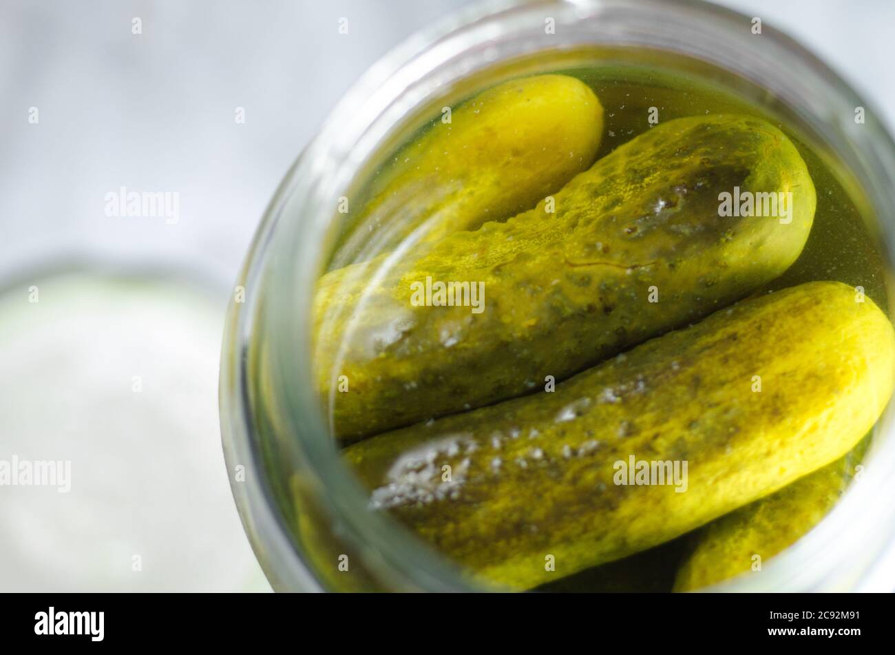 Dill pickles in a glass jar, with the lid out of focus beside the jar leaving some space for copy. Stock Photo