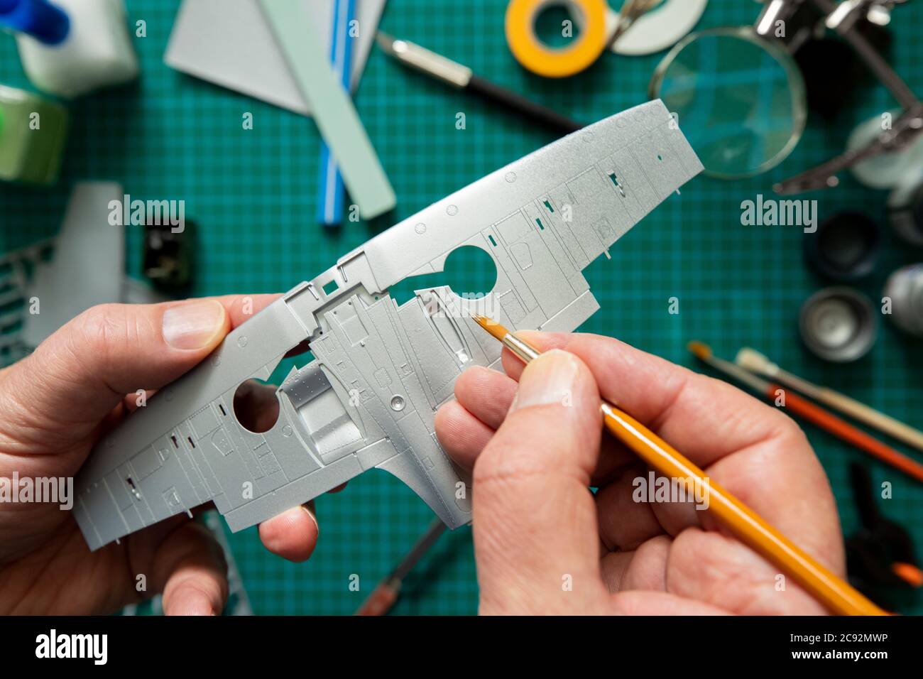 Overhead View Of Man Building Scale Model Aeroplane From Kit On Cutting BoardWith Tools And Materials Stock Photo