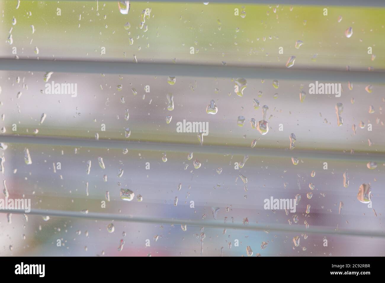 The rain behind a window drips on glass a look through the opening blinds. Stock Photo