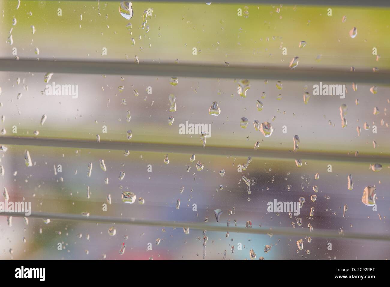 The rain behind a window drips on glass a look through the opening blinds. Stock Photo