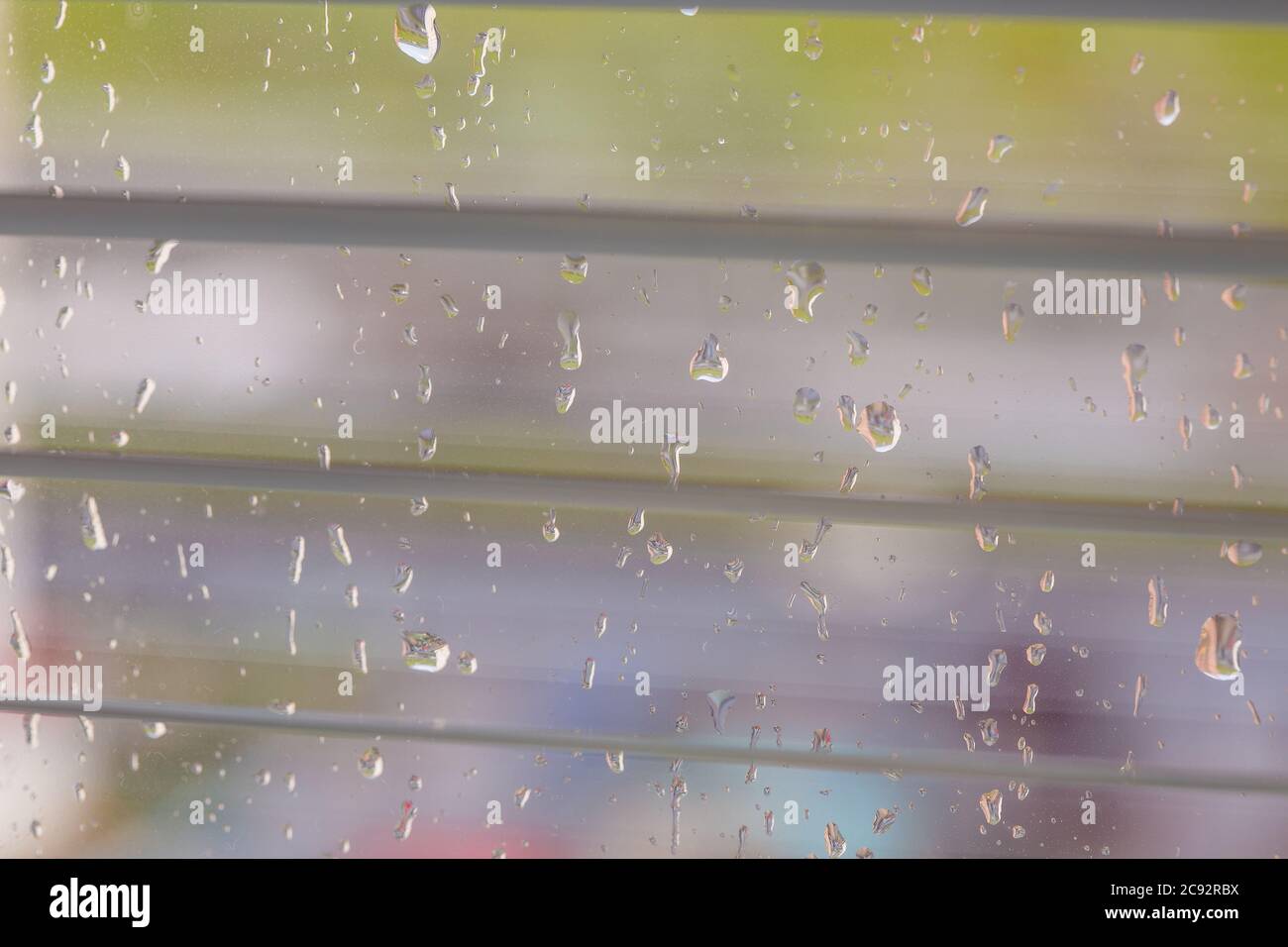 The rain behind a window drips on glass a look through the opening blinds. Stock Photo