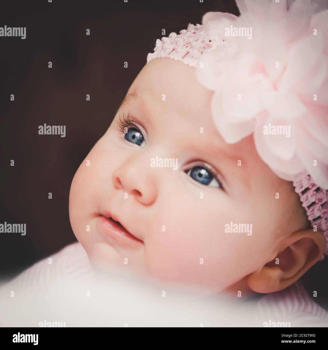 Close-up portrait of cute 3 months old smiling baby girl in pink. Big open eyes. Healthy little kid shortly after birth. Stock Photo