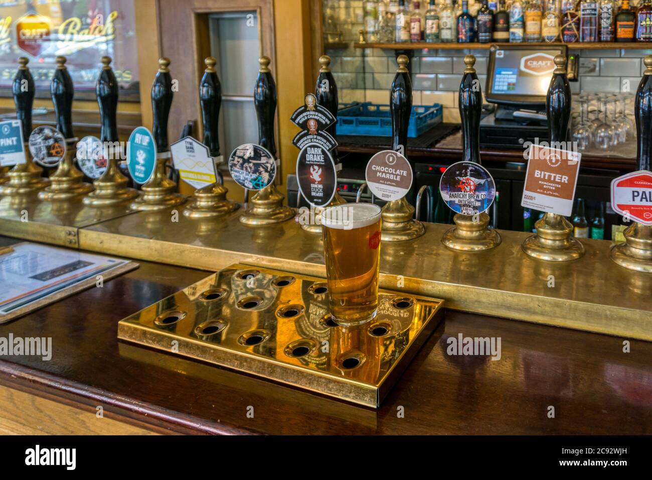 A pint of bitter on a pub bar counter with a large array of pump handles behind. Stock Photo