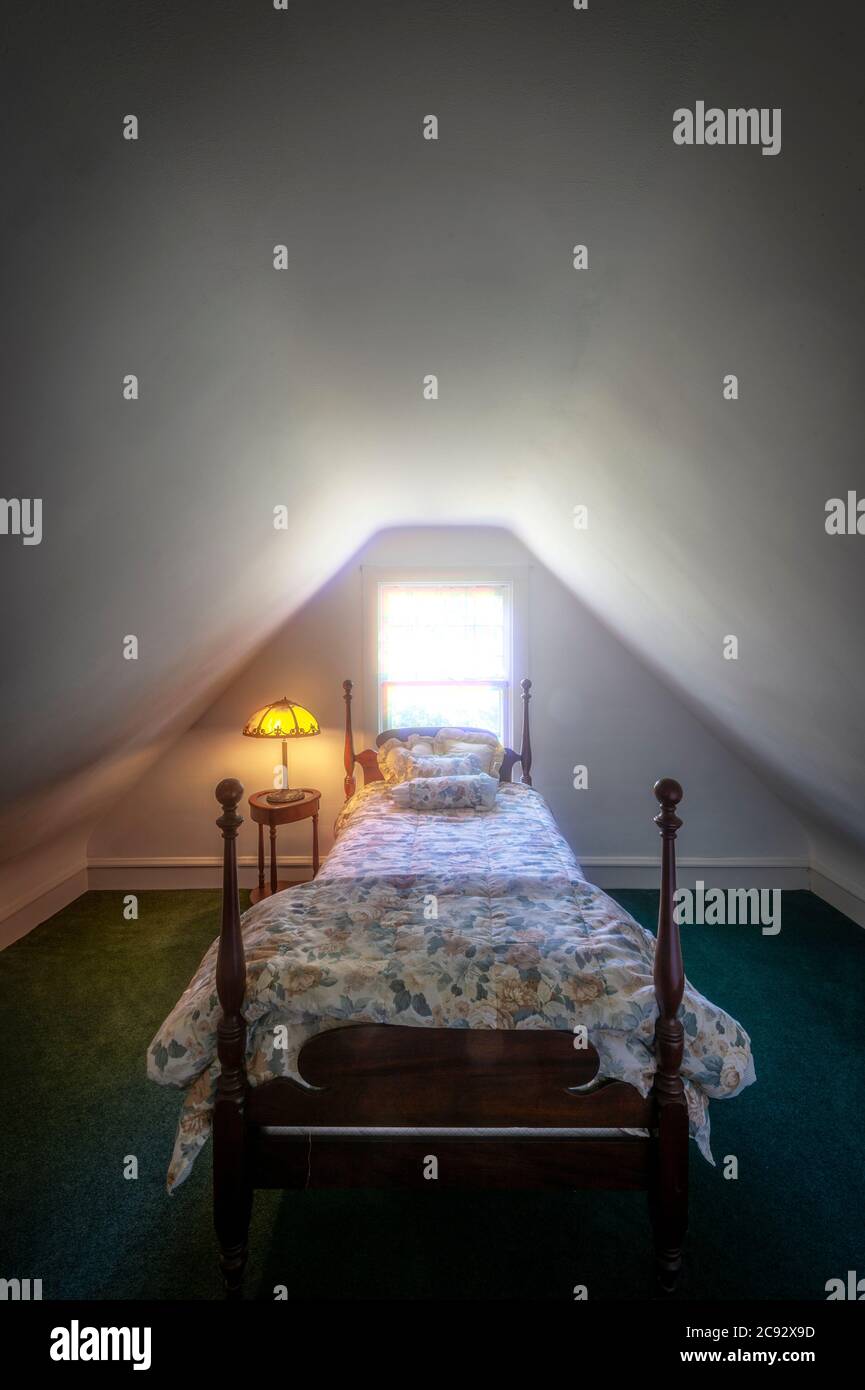 Four post bed in small attic bedroom with light pouring through window. Stock Photo