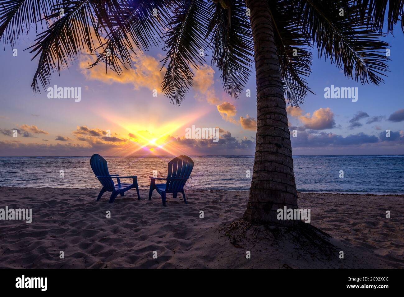 Sunset with sun flare, beach chairs and palm tree. Grand Cayman Island Stock Photo