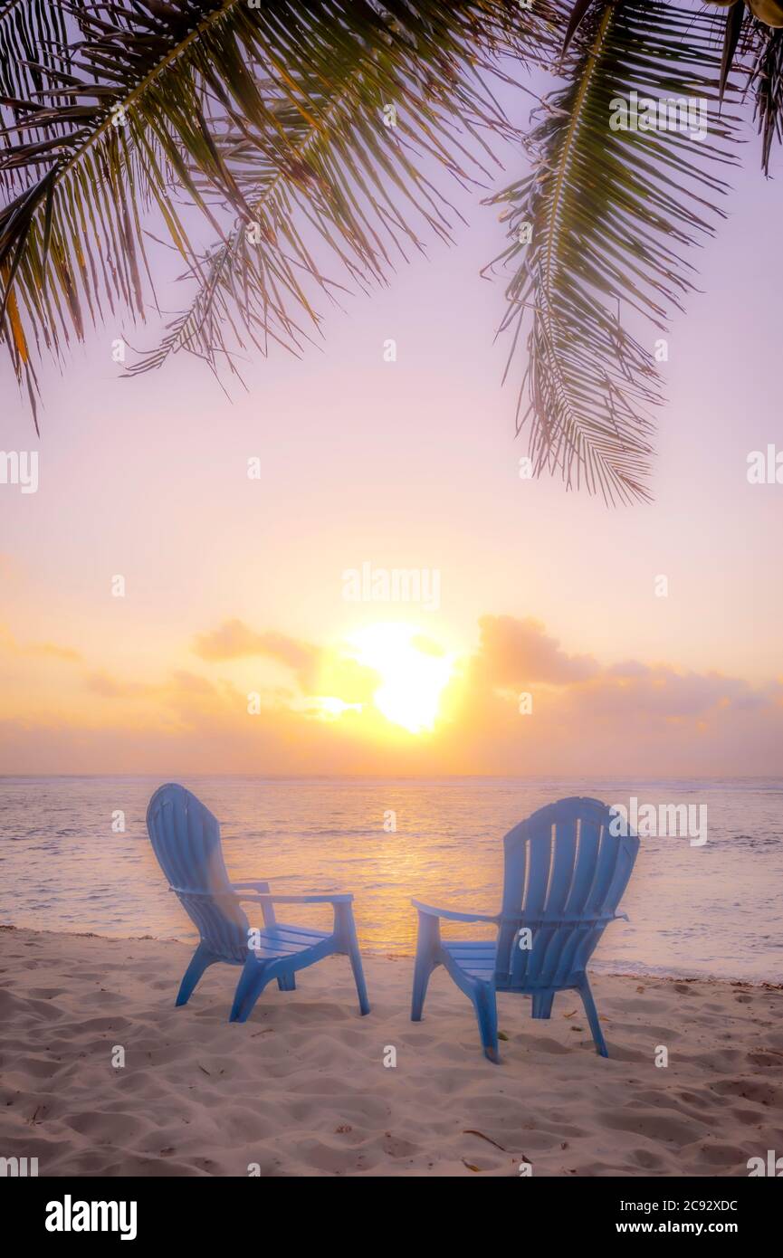 Sunset with sun flare, beach chairs and palm tree. Grand Cayman Island Stock Photo