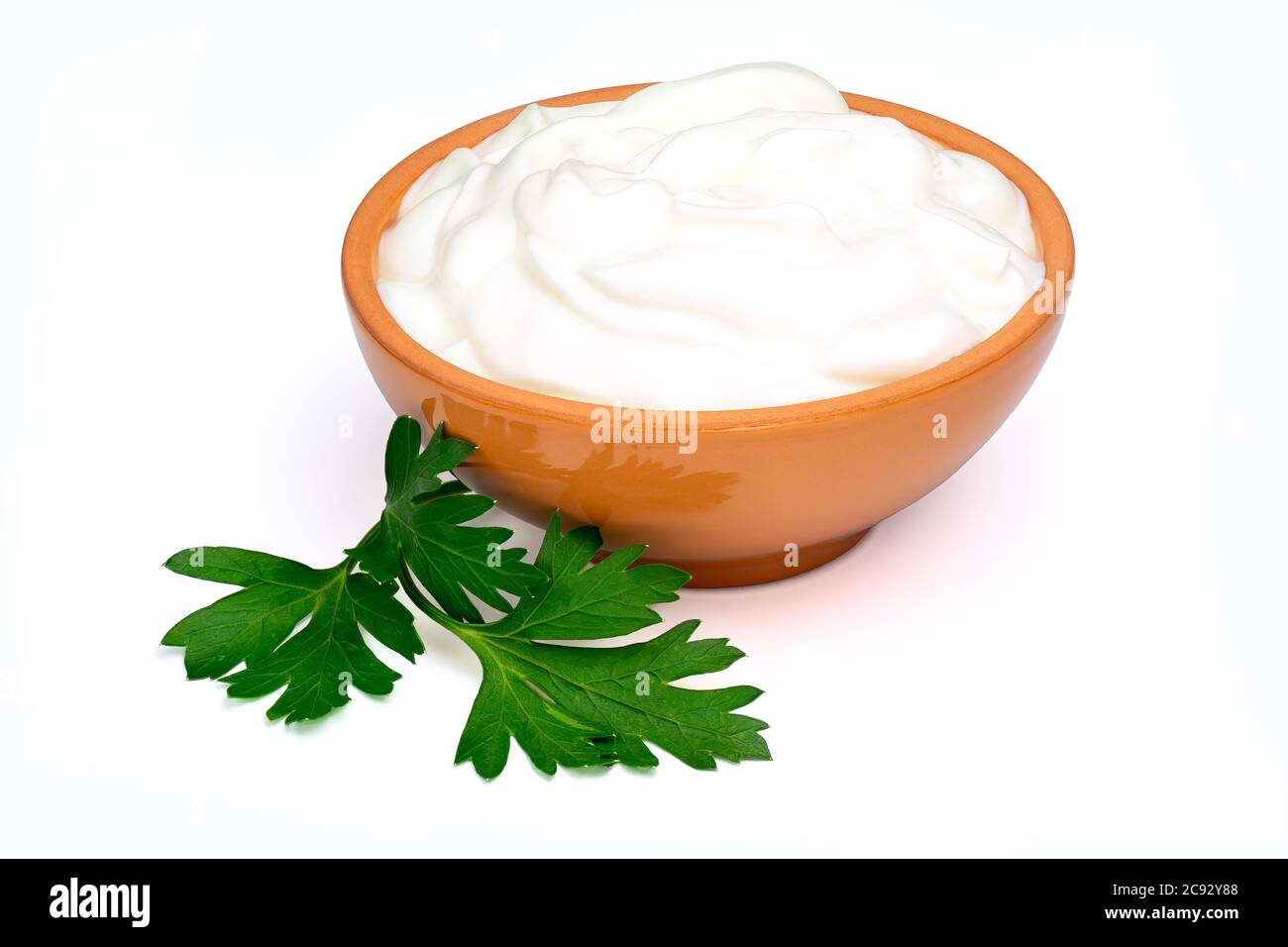 Sour cream, yogurt or soft cottage cheese in a ceramic bowl and parsley leaf isolated on white